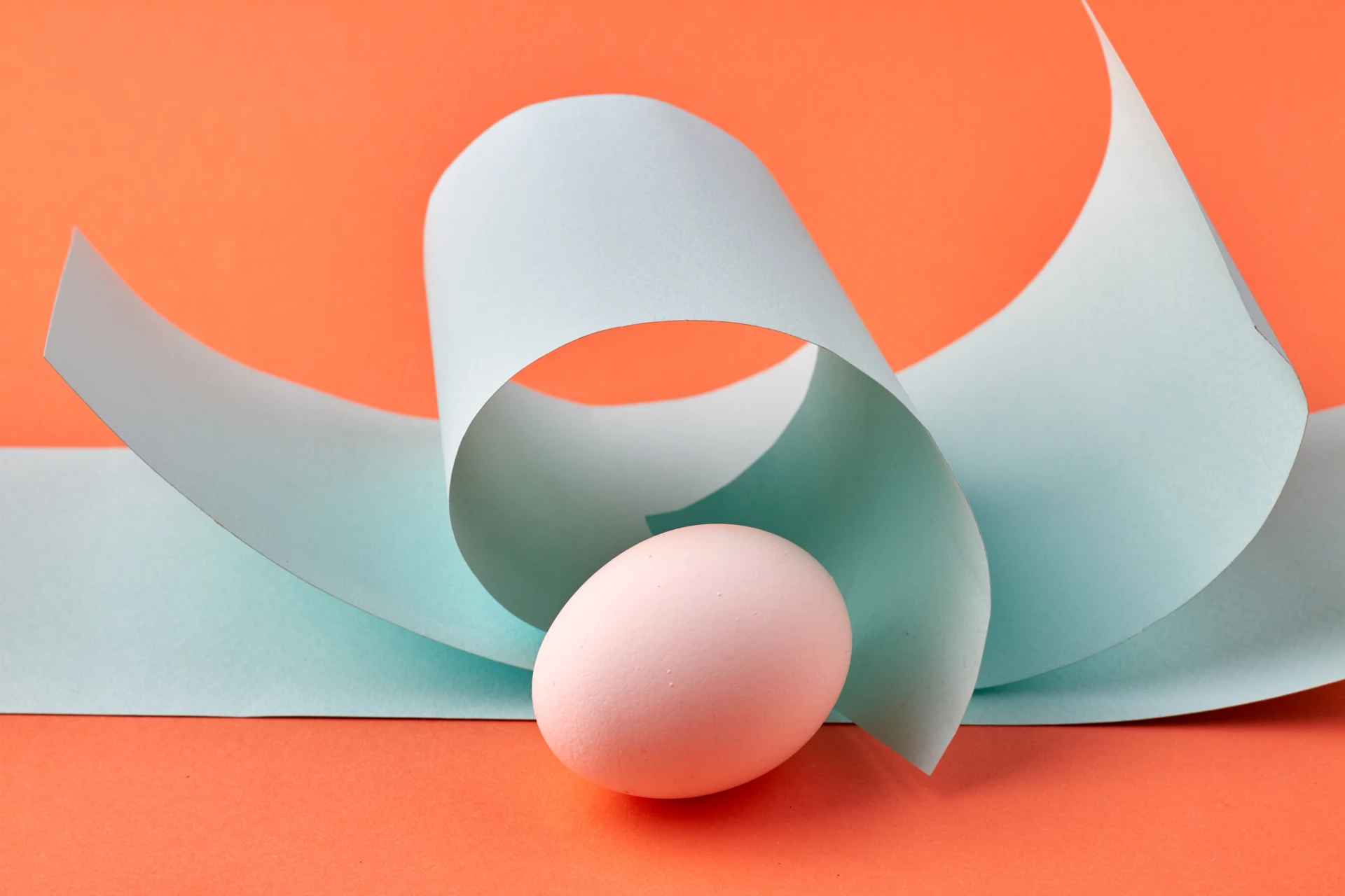 Abstract composition of curved white paper forms and a red sphere against a coral background.