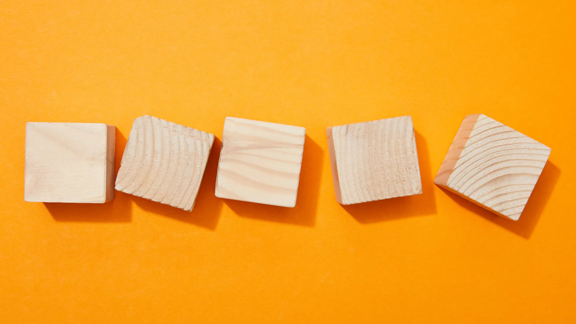 Five wooden blocks angled in different directions on an orange background, representing leadership misalignment.