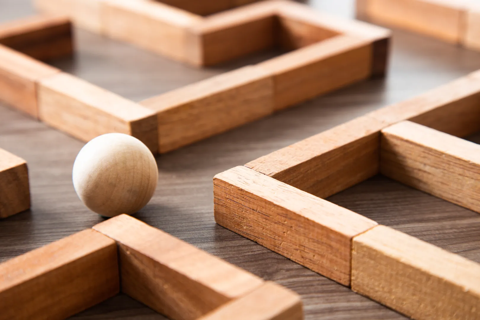 A pale wooden sphere rests at a junction between wooden maze walls.